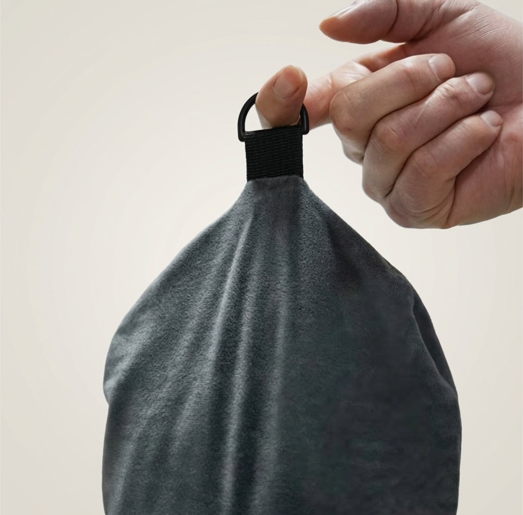 Hand holding a gray fabric bag with a black strap against a light background
